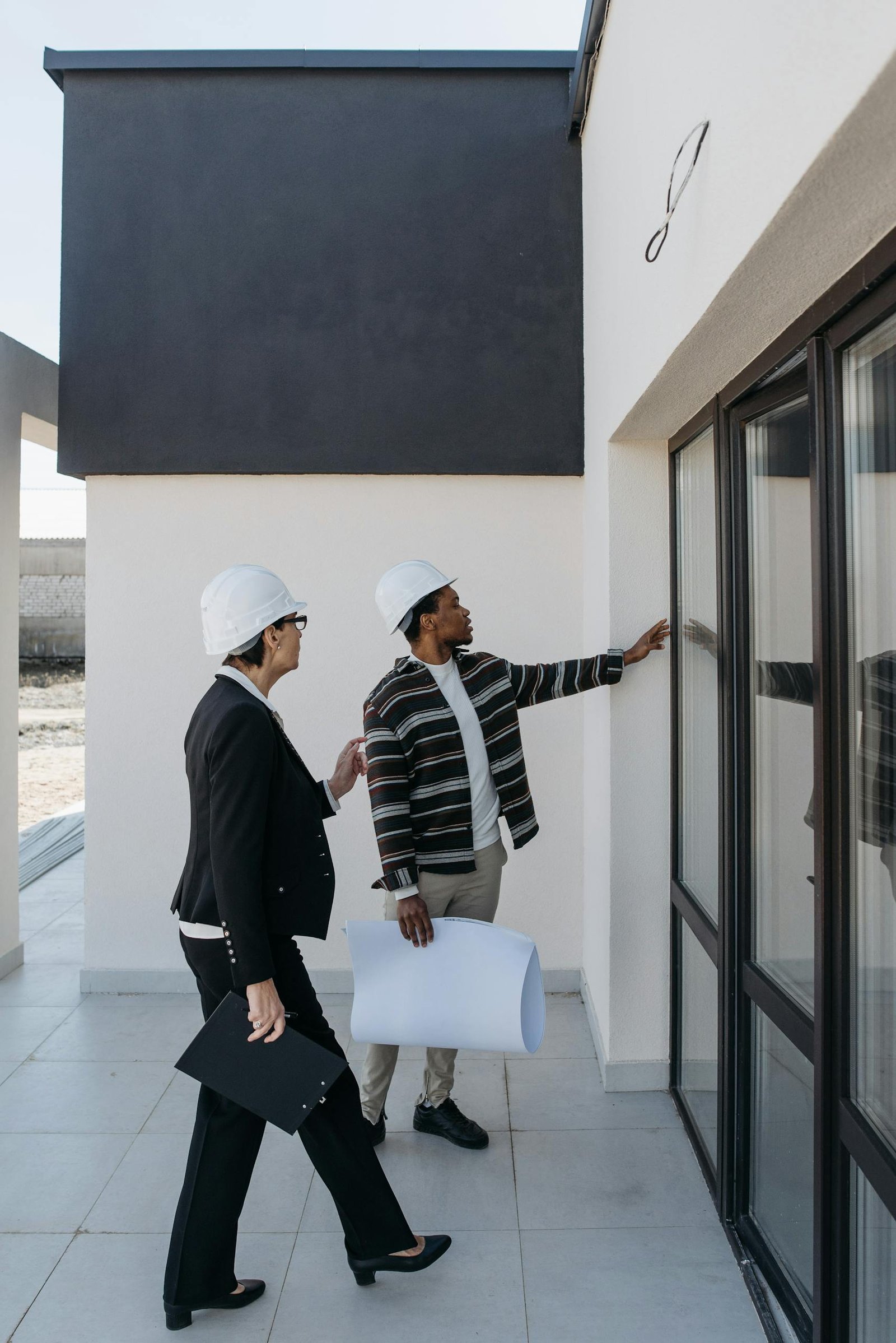 Two architects in hard hats discussing a modern building's glass facade.